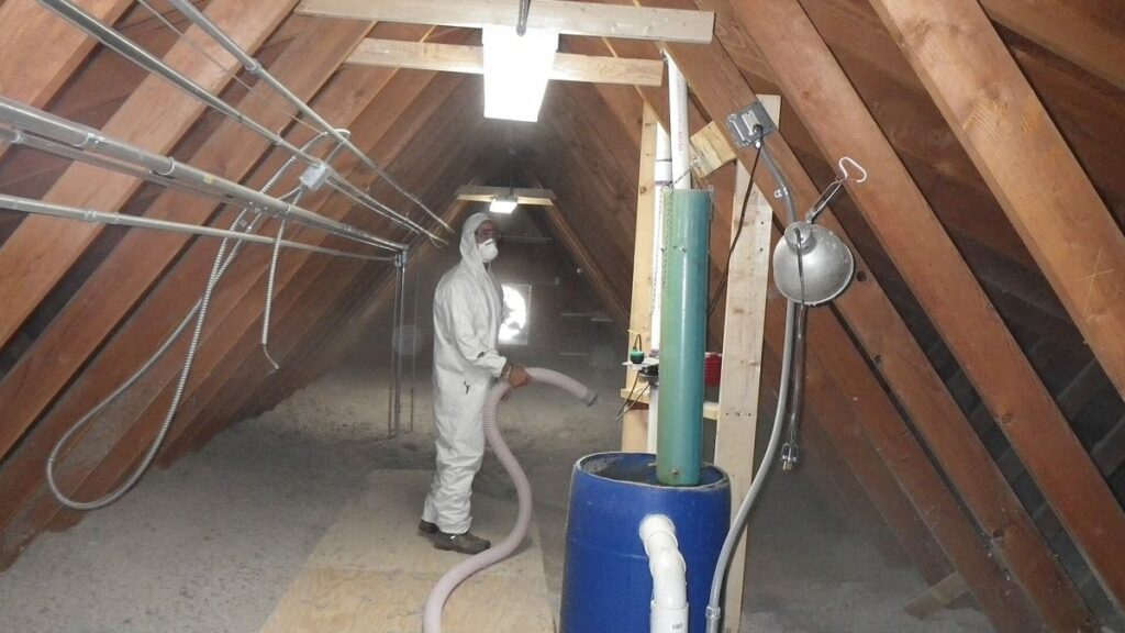 Ouvrier en combinaison soufflant de l'isolant en vrac dans des combles perdus sous charpente bois